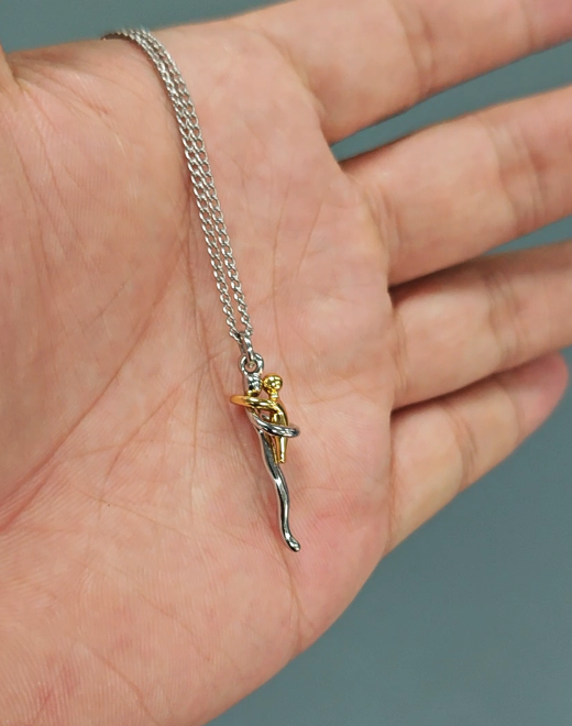 De ketting met de kleine hanger van twee omarmende figuurtjes ligt op een open handpalm, wat het formaat laat zien. 7