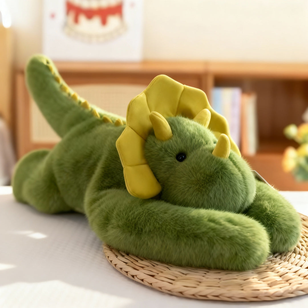 Groene dinosaurus-knuffel met gele kraag en hoorntjes ligt met zijn lange armen voor zich op een rieten onderzetter. 15
