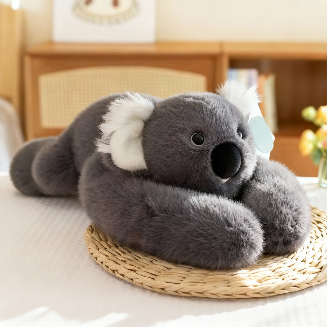 Grijze koala-knuffel met witte oren en een grote zwarte neus ligt met lange armen op een rieten onderzetter. 16
