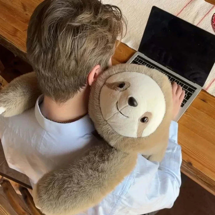 Bovenaanzicht van een man achter een laptop met een luiaard-knuffel die zijn armen om zijn schouders legt. 9