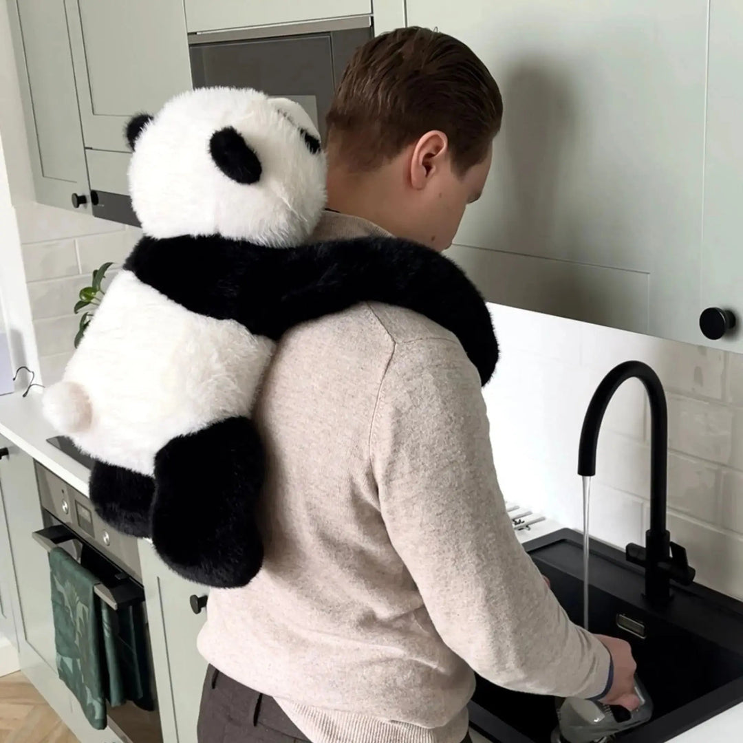 Man staat bij de gootsteen in de keuken met de panda-knuffel op zijn rug, de lange armen om zijn schouders geslagen. 10