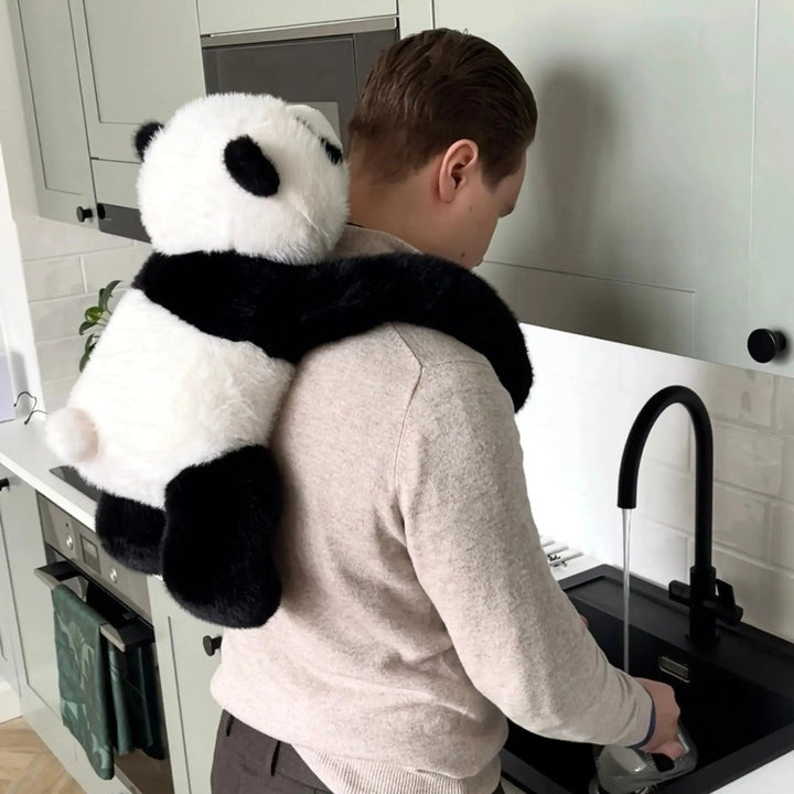 Man staat bij de gootsteen in de keuken met de panda-knuffel op zijn rug, de lange armen om zijn schouders geslagen. 10