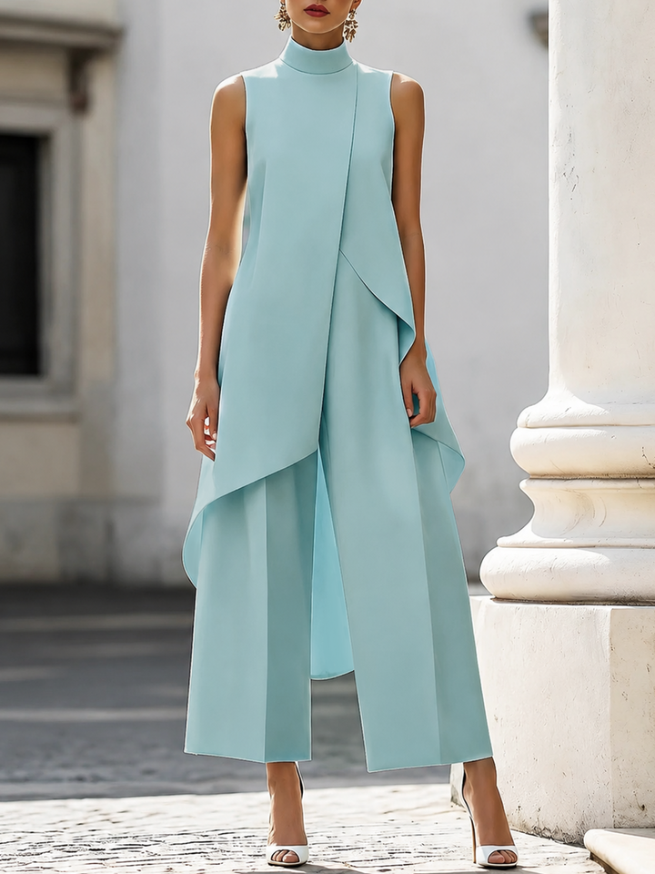 Lichtblauwe set met opstaande kraag, asymmetrische top en wijde broek, gedragen door een model bij een zuil. 4