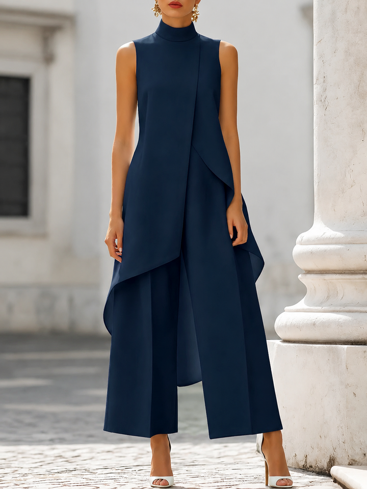Donkerblauwe set met mouwloze asymmetrische top en wijde broek, gedragen door een model op een geplaveide straat. 6