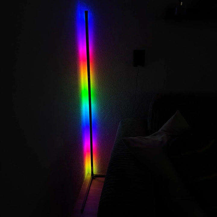 Hoeklamp in een donkere kamer toont een verloop van felle regenboogkleuren op de muur, naast een bank. 6