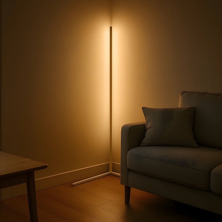 Lichte uitvoering van de hoeklamp straalt warm licht uit in een hoek naast een grijze bank en houten tafel. 7