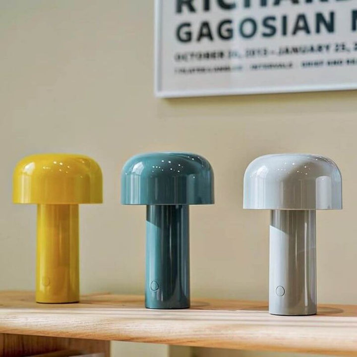 Gele, blauwgroene en lichtgrijze paddenstoellamp naast elkaar op een houten plank onder een ingelijste poster 10