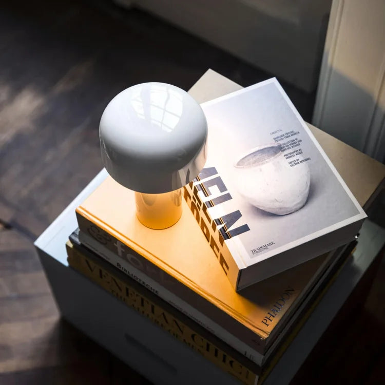 Witte paddenstoellamp met warm licht op een stapel kunstboeken, gezien van boven 20