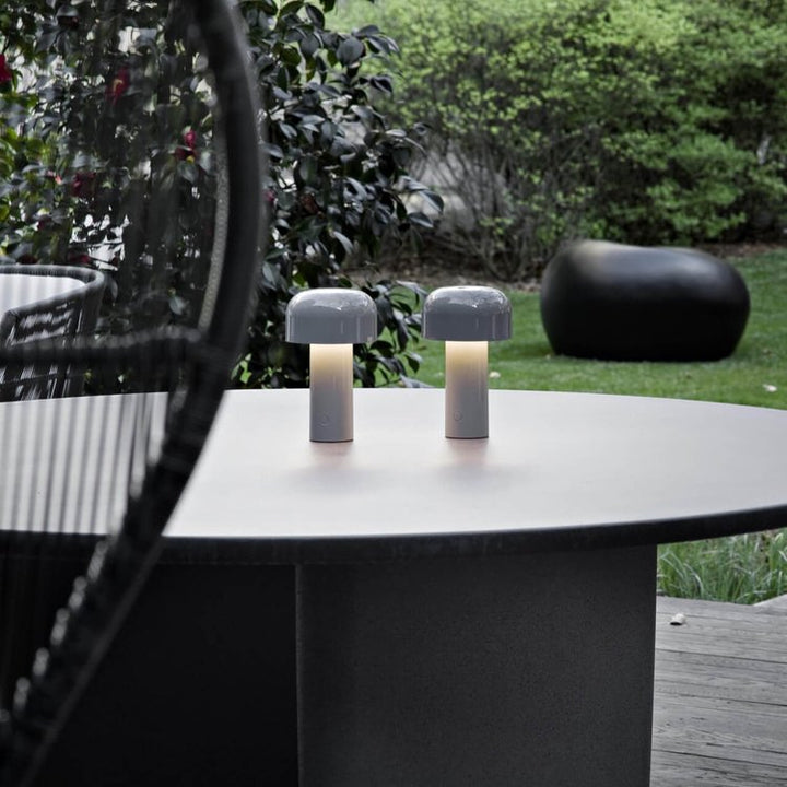 Twee grijze paddenstoellampen staan lichtgevend op een grote ronde buitentafel in de tuin 22