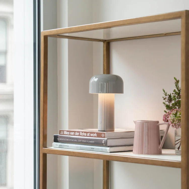 Grijze lamp met gebogen kap staat aan op een stapel boeken in een open kast 23