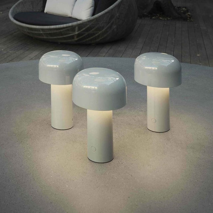 Drie lichtgrijze brandende tafellampen op een ronde betonnen tafel buiten, met een rieten loungestoel op de achtergrond 7
