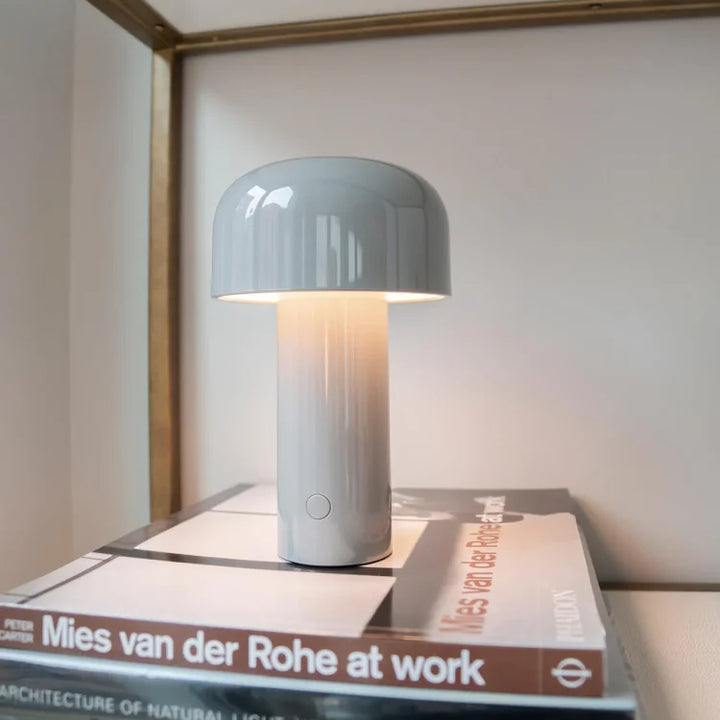 Lichtgrijze brandende tafellamp bovenop een stapel boeken op een plank met een koperkleurig kader 10