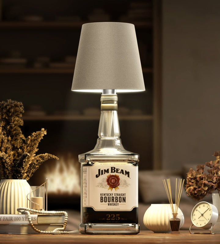 Taupekleurige lampenkap op een vierkante bourbonfles in een gezellige woonkamer met haardvuur, boeken en droogbloemen. 8