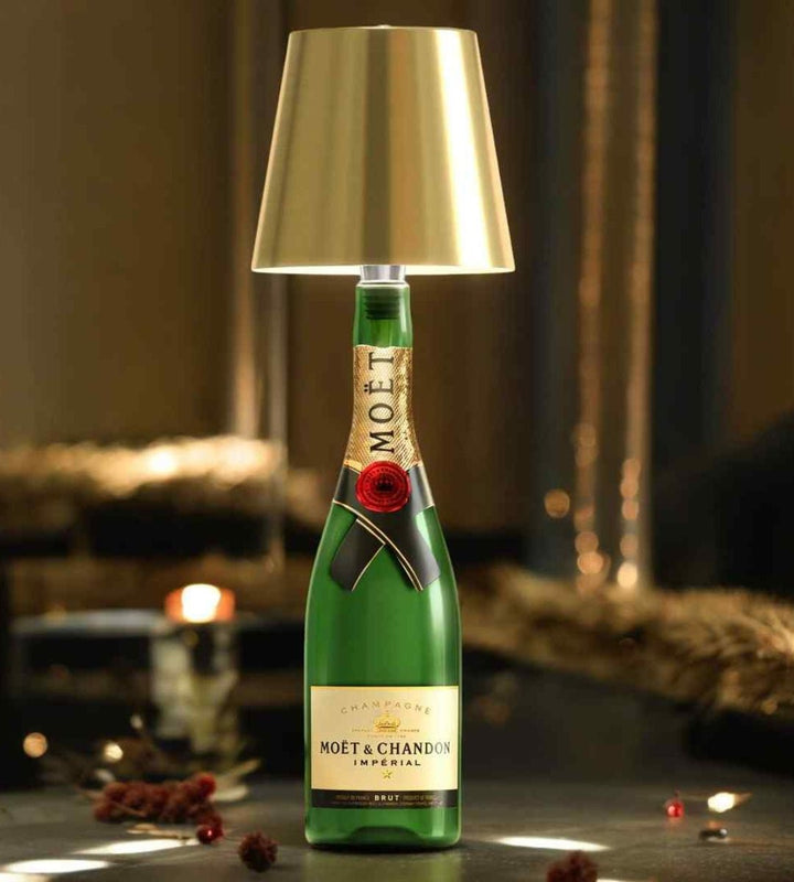 Gouden lampenkap op een groene champagnefles, sfeervol verlicht tussen kerstachtige decoratie op een donkere tafel. 1