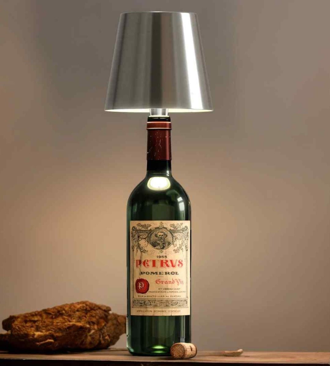 Zilverkleurige lampenkap op een oude groene wijnfles, met een kurk en een brok hout ernaast. 7