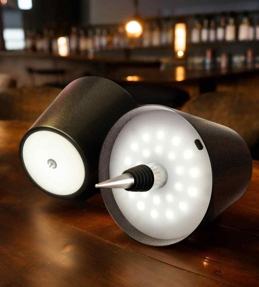 Twee zwarte lampen op hun zij op een houten bartafel, met ledlampjes, flessenstop en aanraakknop zichtbaar. 10
