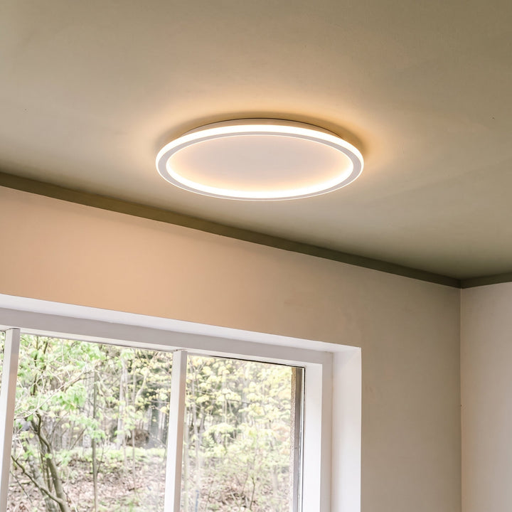 Aangestoken ringlamp aan een plafond naast een wit raam met uitzicht op groen. 8