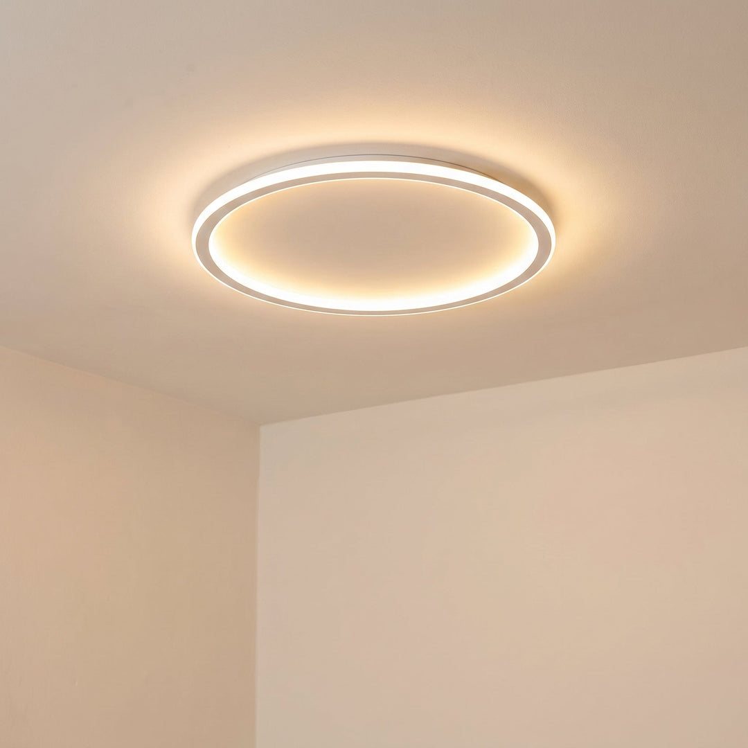 Witte ringlamp op het plafond schuin van onderaf gezien, met een warme gloed tegen de beige muren. 6