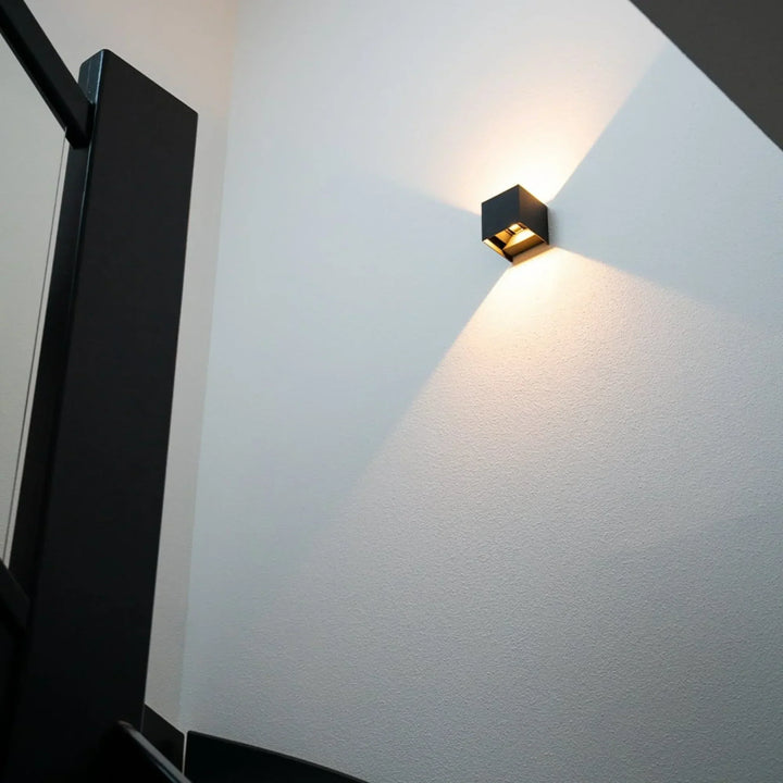 Zwarte wandlamp op een lichte trappenhuismuur naast een zwarte trapleuning, met licht in twee richtingen 8
