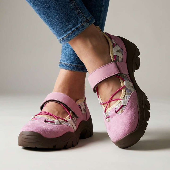 Roze suède instappers met klittenbandband, felroze elastische veters en geruite voering, gedragen met jeans in de studio. 4