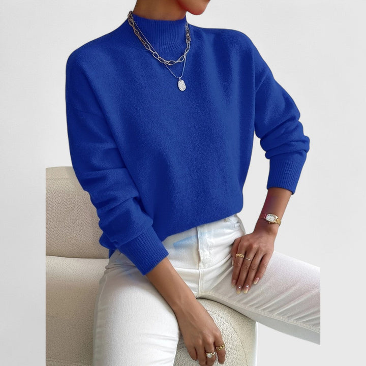 Model draagt de trui in felblauw met ribkraag, gecombineerd met witte broek en zilverkleurige kettingen. 11