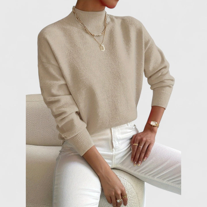 Model draagt de trui in zandbeige met ribkraag, gecombineerd met witte broek en gouden kettingen en horloge. 7