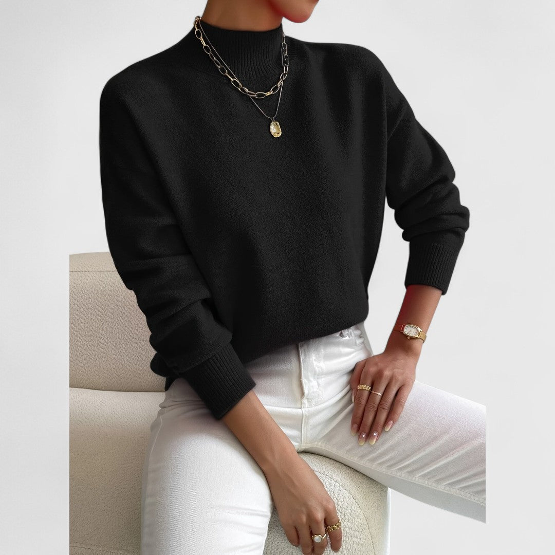 Model draagt de trui in zwart met ribkraag en manchetten, met witte broek en gouden kettingen als contrast. 8