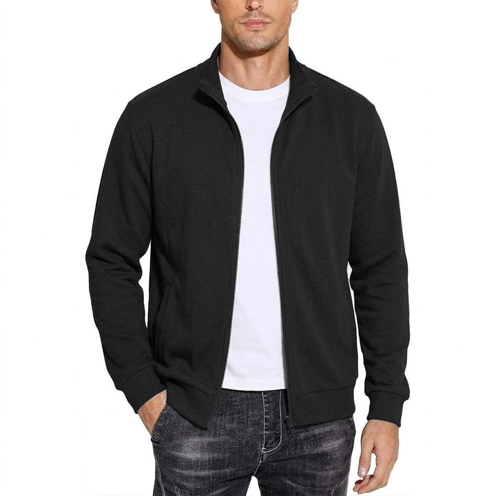 Model draagt de sweatjack in zwart, open ritssluiting over een wit T-shirt, opstaande kraag, een hand in de zak. 1