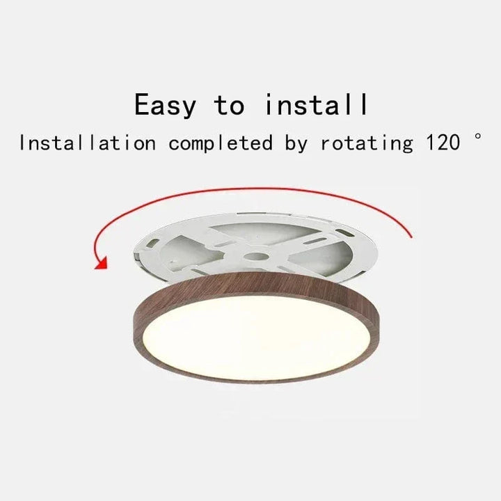 Ronde plafondlamp met donkere houtlook rand boven de witte montageplaat, rode pijl toont de draaibeweging voor eenvoudige installatie. 1