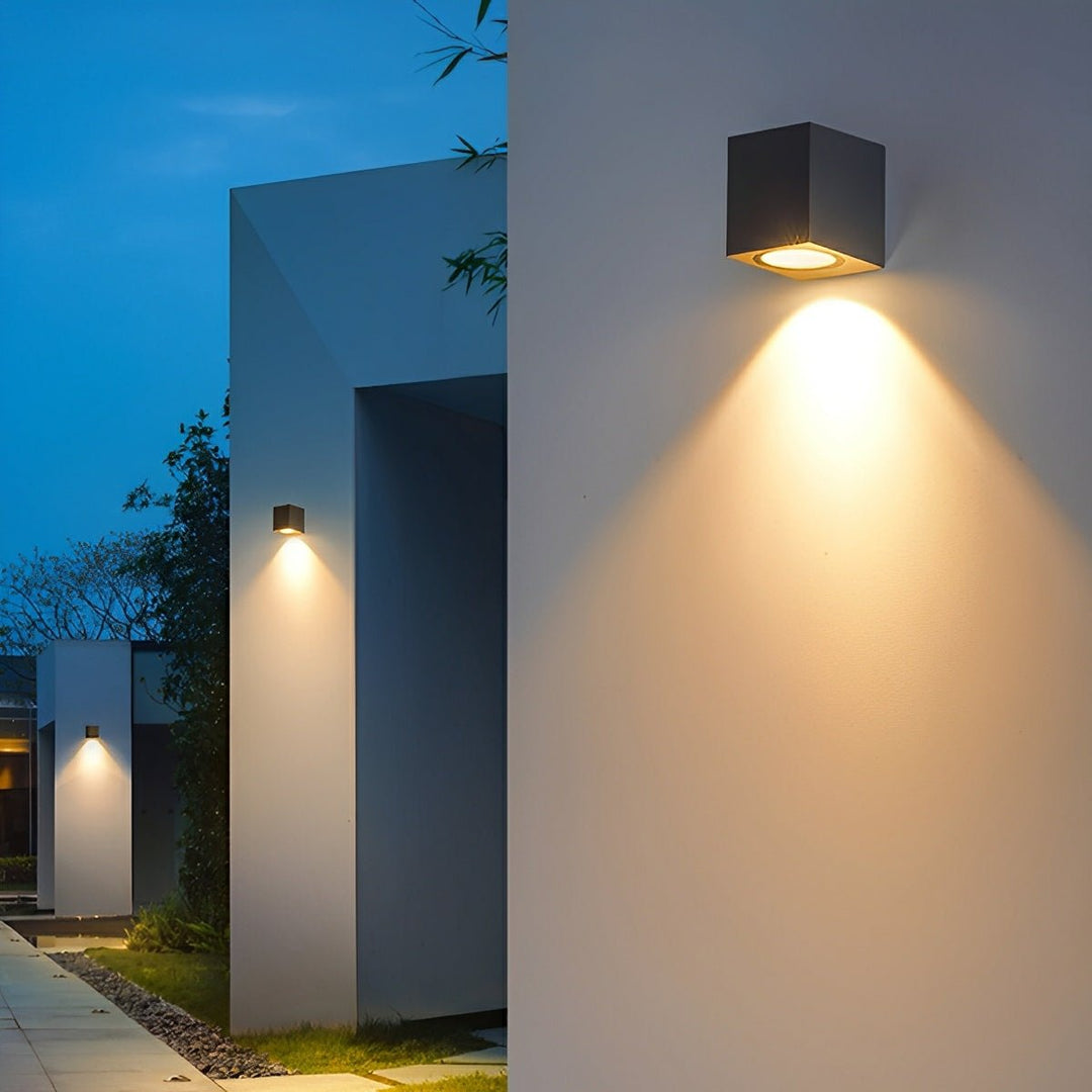 Zwarte kubuslampen met neerwaarts licht langs een witte gevel en tuinpad bij avondlicht 6