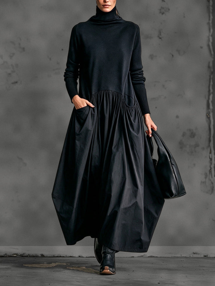 Model in zwarte maxi-jurk met opstaande kraag, hand in de zak, zwarte tas en laarzen 1