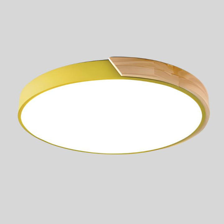 Gele ronde plafondlamp met houten accent aan de rand, vrijstaand getoond op een lichtgrijze achtergrond. 15