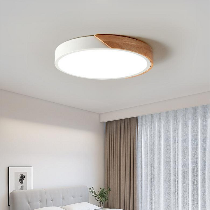 Witte ronde plafondlamp met houten accent aan de rand, brandend in een slaapkamer met bed en gordijnen. 3