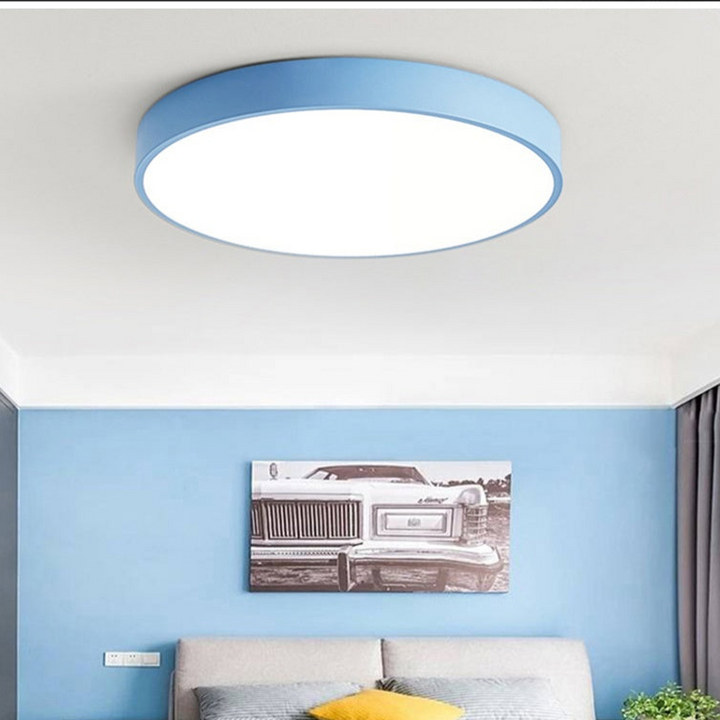 Lichtblauwe ronde plafondlamp zonder houten accent boven een bed in een slaapkamer met blauwe muur en schilderij. 4