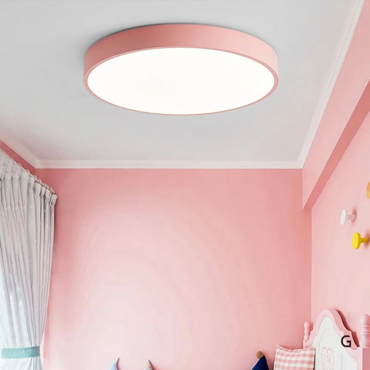 Roze ronde plafondlamp zonder houten accent in een roze kinderkamer met gordijn en bedhoofdeinde. 5