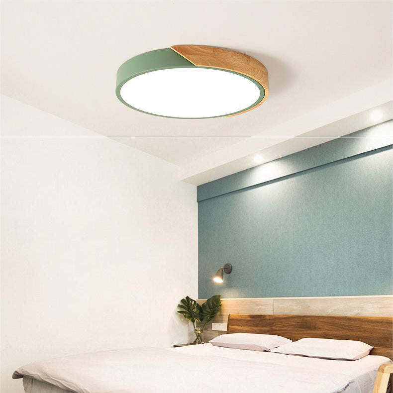 Groene ronde plafondlamp met houten accent aan de rand, boven een slaapkamer met houten hoofdbord en blauwgroene muur. 6