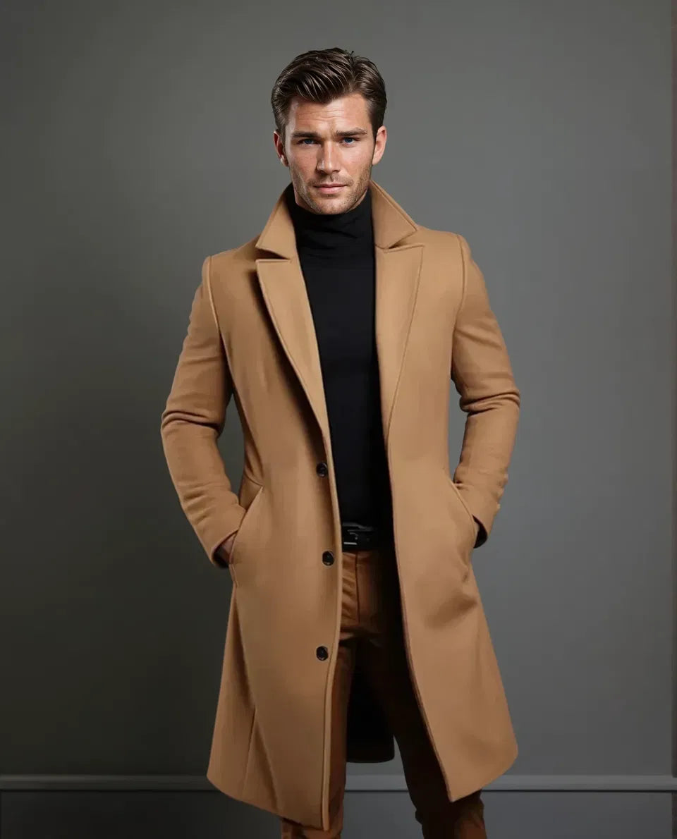 Heel gezicht en volledige lengte: model in kameelbruine overjas met zwarte coltrui, bruine broek en riem, handen in de zakken. 5