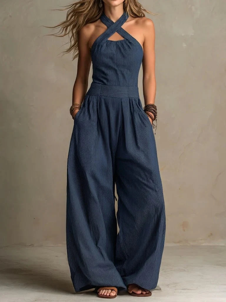 Model draagt de jumpsuit in donkerblauw met fijn streepje, gekruiste halsbandjes, zakken en ruim vallende pijpen. 3