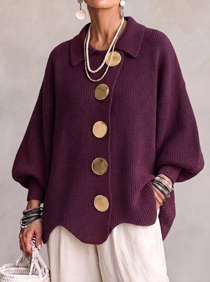 Het gebreide vest in donker aubergine met grote goudkleurige knopen, gedragen met parelkettingen, wijde witte broek en rieten tas. 2