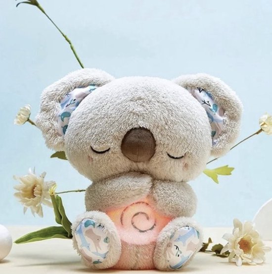 Pluche koala met gesloten ogen en gevouwen pootjes, met een zacht roze gloeiende spiraal op de buik, tussen witte bloemen. 1