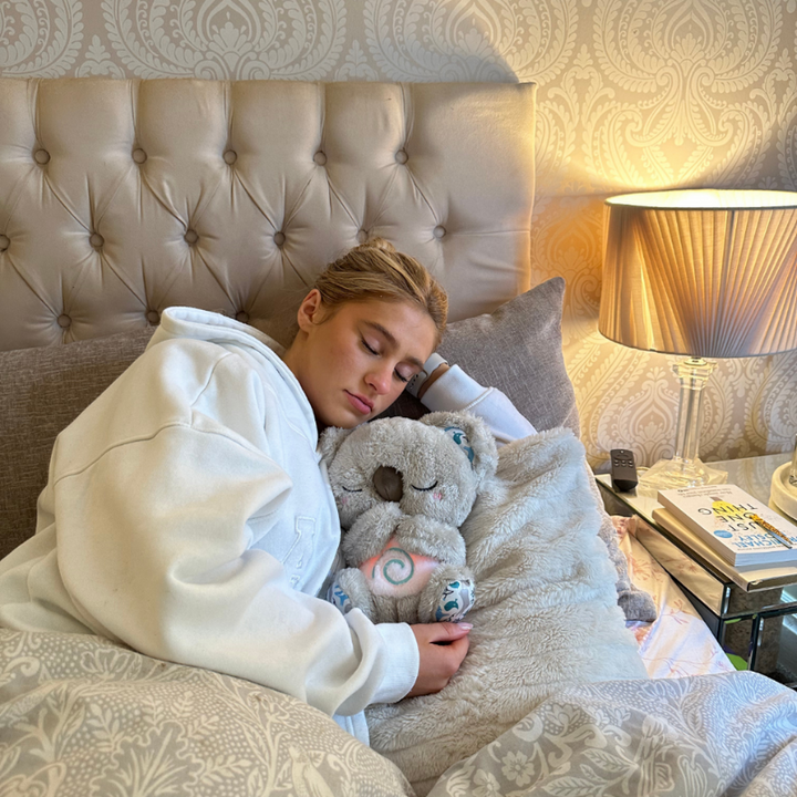 Slapende jongere in witte hoodie die in bed een grijze pluche koala met roze gloeiende spiraal op de buik vasthoudt. 14