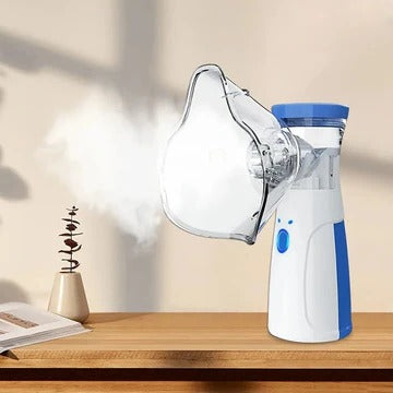 Wit-blauwe handvernevelaar met masker op een houten tafel, met een fijne damp die uit het masker komt, naast een boek. 1