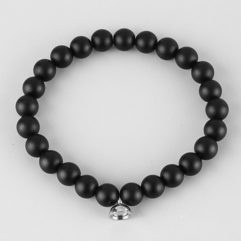Armband van matzwarte kralen met klein zilverkleurig magneetbedeltje, bovenaanzicht op lichtgrijze achtergrond 2