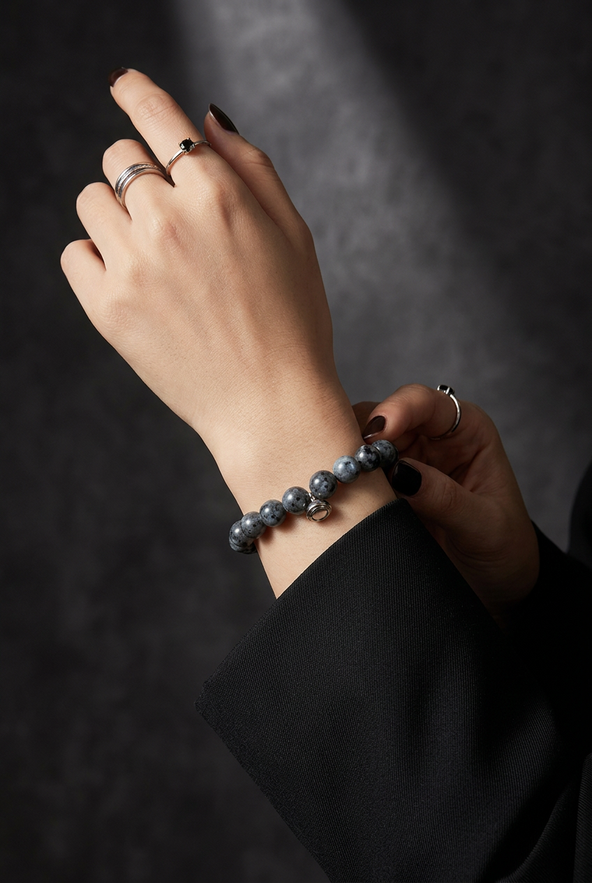 Pols van een model met de grijsblauwe kralenarmband, gecombineerd met zilverkleurige ringen en een zwarte mouw 4