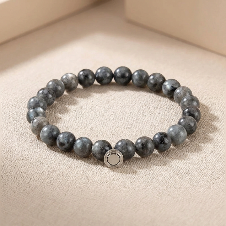 Armband van grijsblauwe gevlekte stenen met een rond zilverkleurig magneetsluitingsdeel, liggend op een beige doek 3