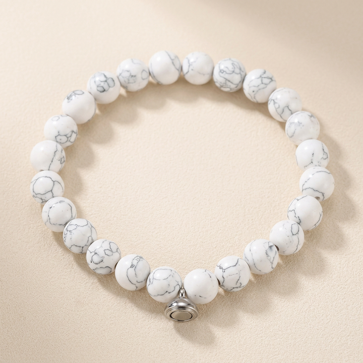 Armband van witte kralen met grijze adering en een zilverkleurige magneetsluiting op beige achtergrond 2