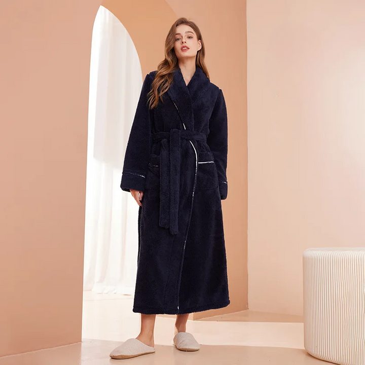 Model in marineblauwe lange badjas met ceintuur, frontaal, in een abstract perzikkleurig interieur met pantoffels 1