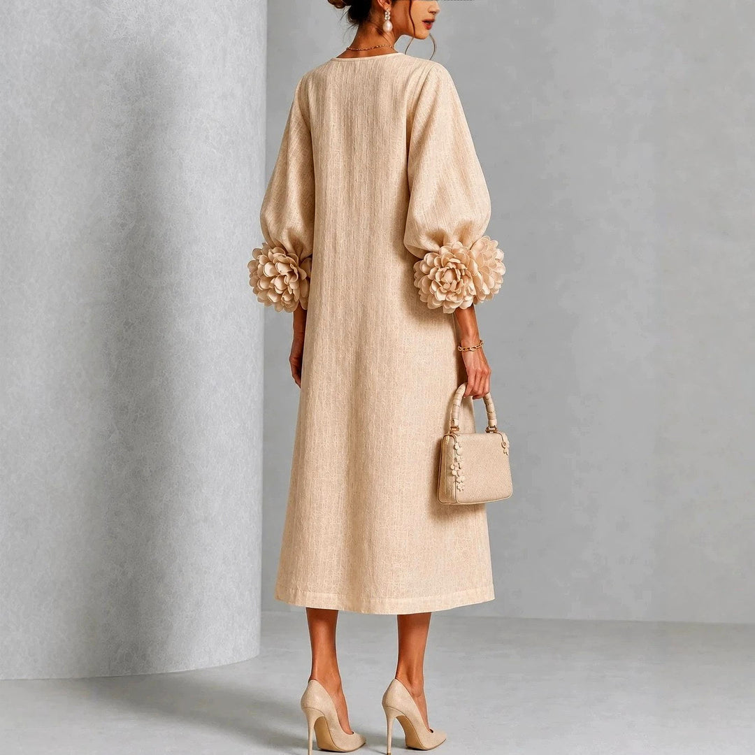 Achteraanzicht van de beige jurk op een model, met rechte rug, pofmouwen en grote bloemenmanchetten, plus een beige handtas. 5
