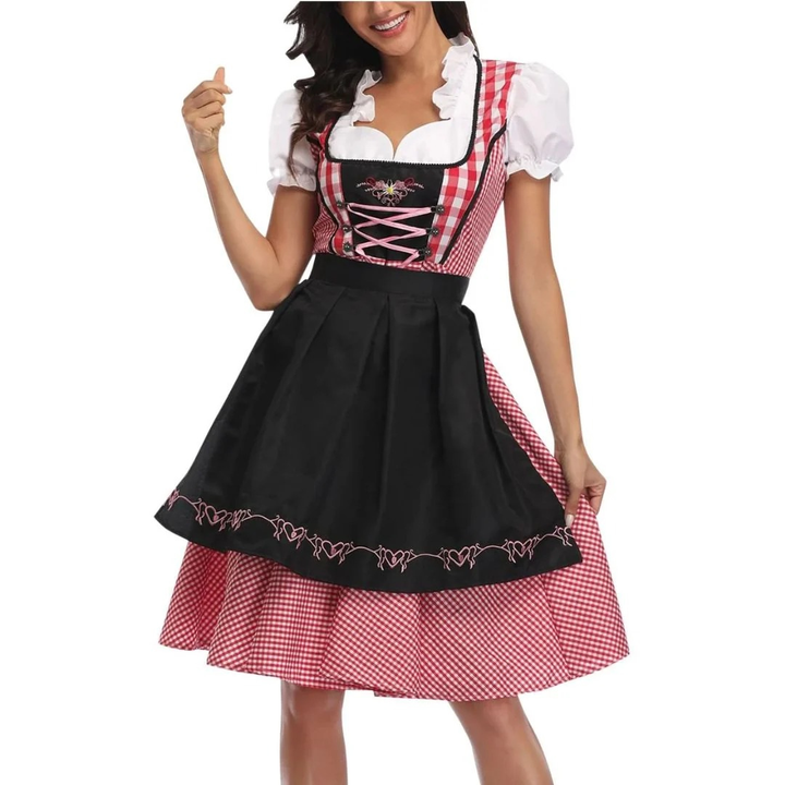 Model draagt de rood-wit geruite dirndl met zwarte schort, roze vetersluiting en witte pofmouwen, van voren gefotografeerd. 1
