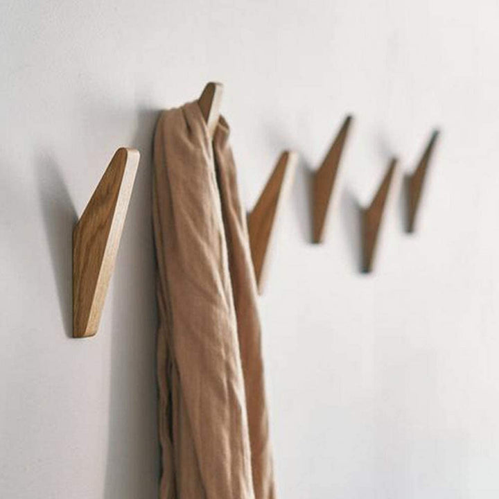 Rij houten haken aan een witte muur, waarvan een haak een beige sjaal draagt. 2